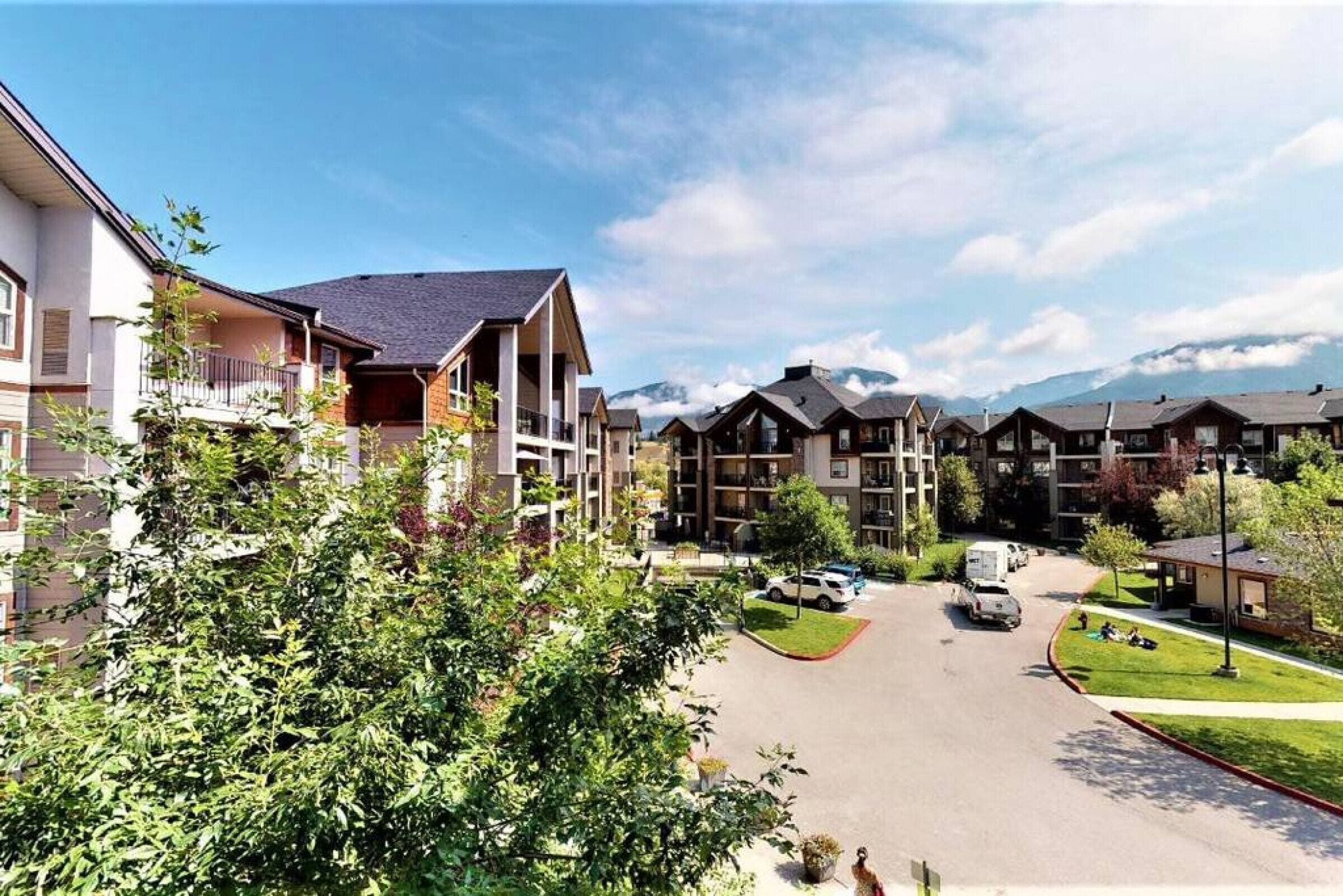 A residential area with modern multi-story buildings, a central road, and a mountain backdrop.