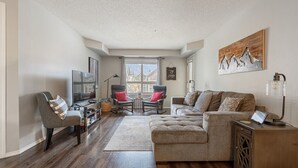 A living room with a sofa, chairs, a TV, and a painting on the wall.