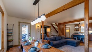 Ein geräumiger Wohnbereich mit einem Holzespeisetisch, der für eine Mahlzeit gedeckt ist, einem blauen Sofa und einer Treppe zu einer weiteren Ebene.