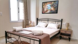 A neatly made bed with white linens and towels, a bedside table with a lamp, and a painting of a garden on the wall.