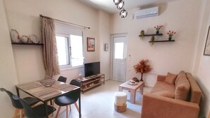 A living room with a sofa, a TV, a dining table with chairs, and a small side table.