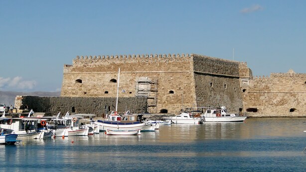 A historic stone fortress with a moat, surrounded by calm water with several boats docked.