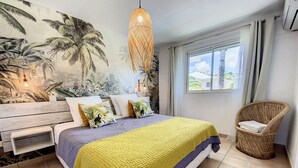 A bedroom with a bed, a chair, a window, and a wall mural. - Villa Zandoli – Private Pool Just Steps from Orient Bay Beach, 3 bedrooms (Orient Bay)