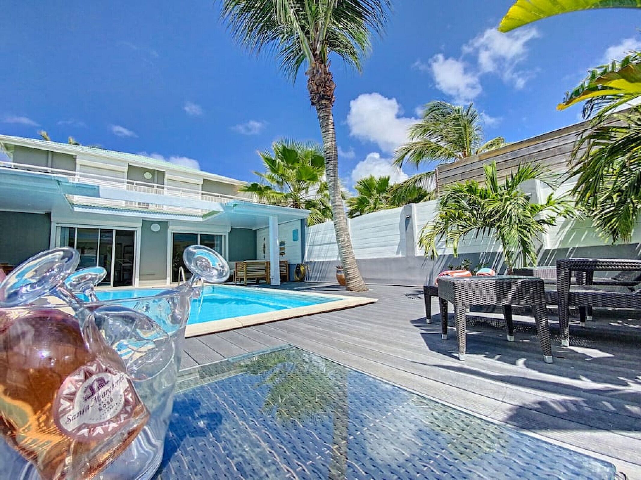 A pool area with a glass table, lounge chairs, and a palm tree.