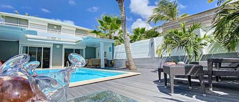 A pool area with a glass table, lounge chairs, and a palm tree.