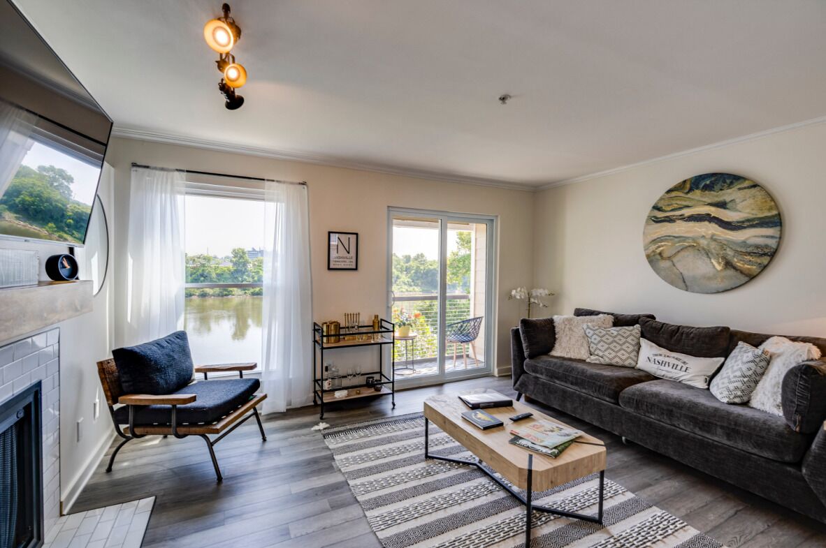 A living room with a fireplace, a sofa, a coffee table, and a view of a lake through large windows.
