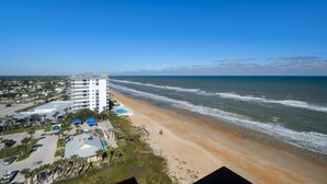 A coastal hotel with a beach view, parking area, and a pool.
