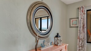 A room with a round mirror, a pink vanity, a decorative anchor sign, and a framed picture on the wall.