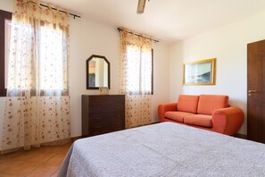 Ein Schlafzimmer mit einem Bett, einem Schminktisch, einem orangefarbenen Sofa, einem Spiegel und einem Bild an der Wand.