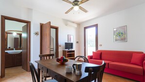 Uma área de refeições com uma mesa de madeira, cadeiras, um sofá vermelho e um ventilador de teto.