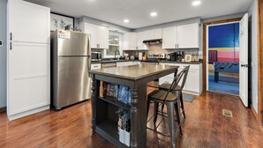 A modern kitchen with white cabinets, a stainless steel refrigerator, and a wooden island with chairs. - Family Fun Hocking Hills Retreat, 2 Decks, Game Rm (Logan)