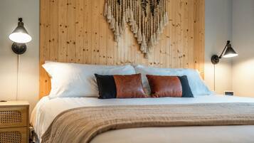 Una cama bien hecha con almohadas blancas y marrones, un cabecero de madera y un tapiz con borlas colgado en la pared.