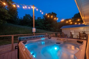 Un jacuzzi con luces LED azules, rodeado por una terraza de madera y luces colgantes.