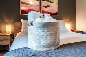 Un lit bien fait, avec un grand panier en osier rempli de serviettes blanches, dans une chambre d’hôtel.