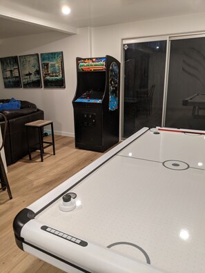 A pool table in a room with a game console and artwork on the wall.
