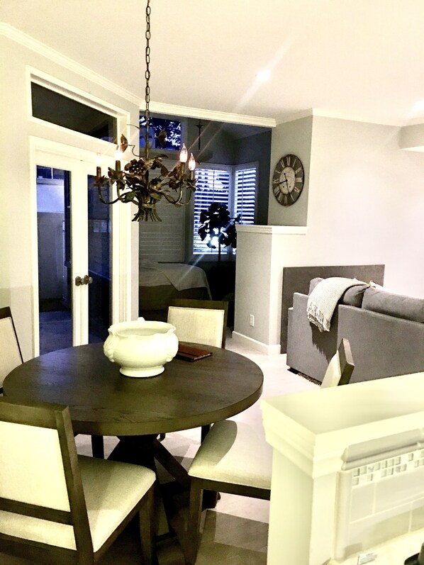 A dining area with a round table, chairs, a chandelier, and a clock on the wall.