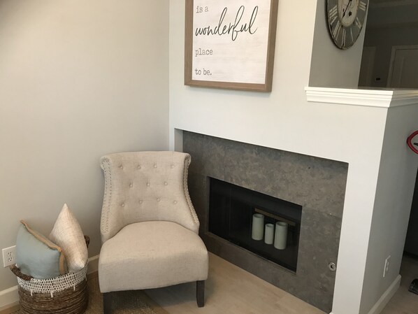 Una habitación con chimenea, un sillón con cojines y un reloj en la pared.