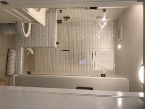 A modern bathroom with white tiled walls and floor, a shower area, a towel rack, and a small sink.