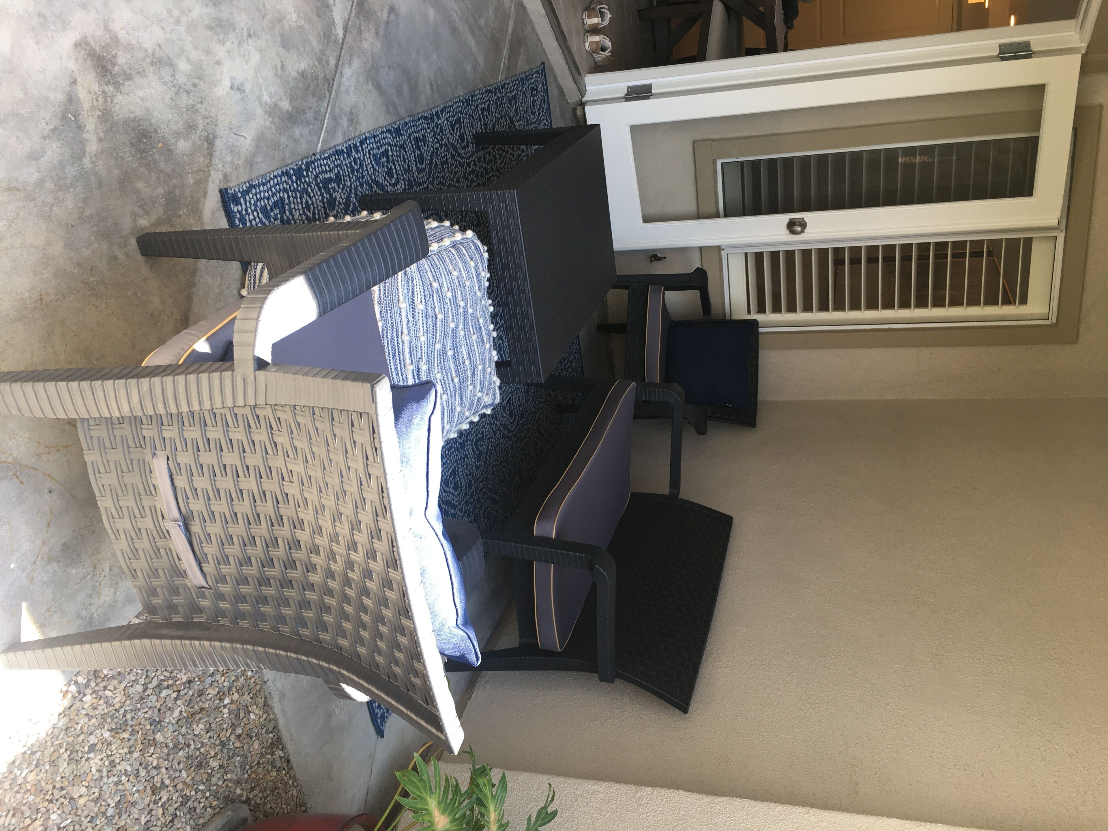 Una habitación con un ventanal grande, un aire acondicionado blanco, una silla de mimbre y un tapete azul con estampado.