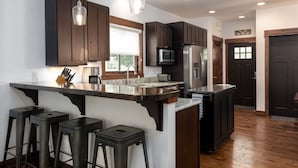 Une cuisine moderne avec des meubles de rangement en bois foncé, un réfrigérateur en acier inoxydable, un four à micro-ondes et un grand îlot central doté de tabourets de bar.