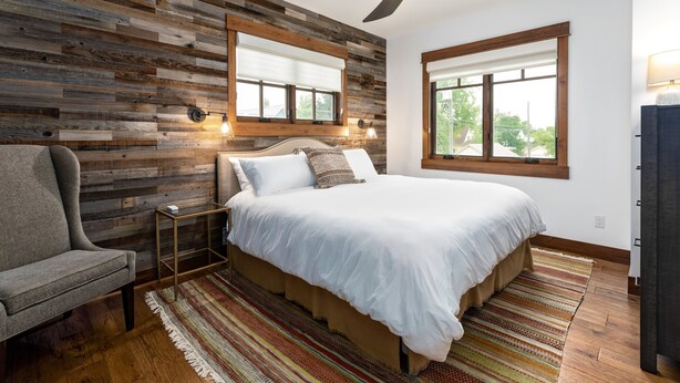 Une chambre avec un mur en bois, un lit avec une literie blanche, une chaise, une table de chevet et une fenêtre donnant sur un paysage.