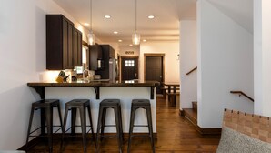 Une cuisine moderne avec des meubles en bois foncé, un îlot central doté de tabourets de bar, un éclairage suspendu et un escalier menant à un autre niveau.