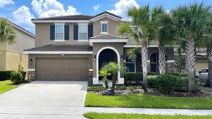 A two-story house with a garage, a covered entryway, and a well-maintained lawn with palm trees. - Crisp & Pristine Pool & Spa & Game Room Home! Solterra Resort! (Davenport)