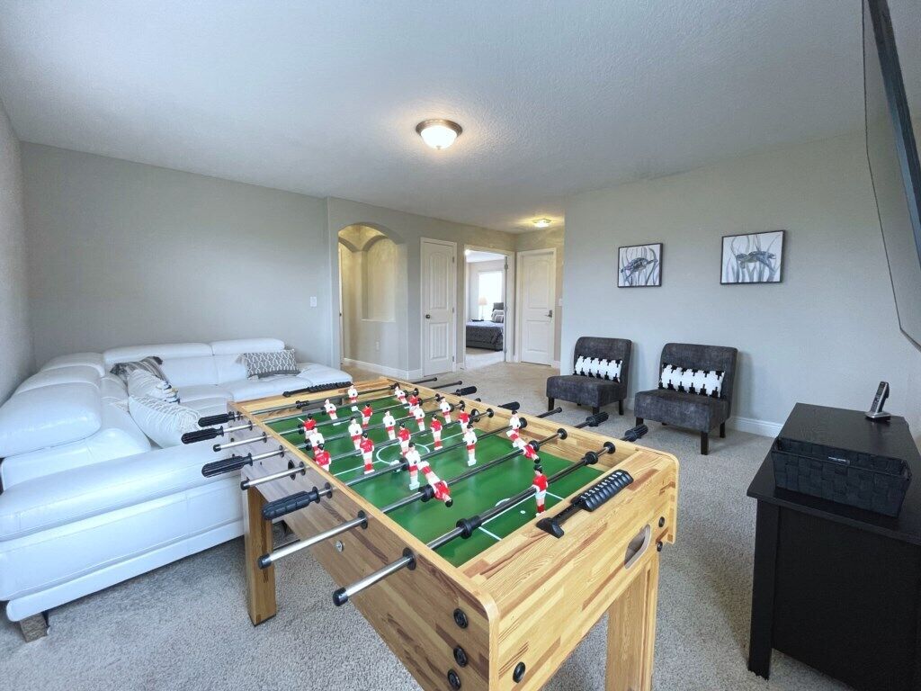 Een kamer met een tafelvoetbaltafel, een witte bank, twee fauteuils en een zwarte tafel met een afstandsbediening.