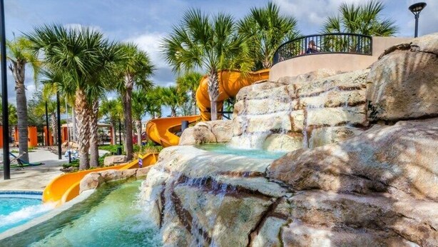 A water park with a large rock formation, a pool, and palm trees. - Crisp & Pristine Pool & Spa & Game Room Home! Solterra Resort! (Davenport)