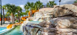 A water park with a large rock formation, a pool, and palm trees. - Crisp & Pristine Pool & Spa & Game Room Home! Solterra Resort! (Davenport)