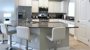 A modern kitchen with white cabinets, a granite countertop, stainless steel appliances, and a bar area with stools. - Crisp & Pristine Pool & Spa & Game Room Home! Solterra Resort! (Davenport)