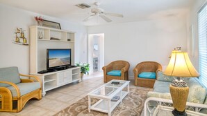 A living room with a television, two wicker chairs with blue cushions, a white coffee table, and a floor lamp. - Baywatch Cabin- Boat Dock on the Channel (Captiva)