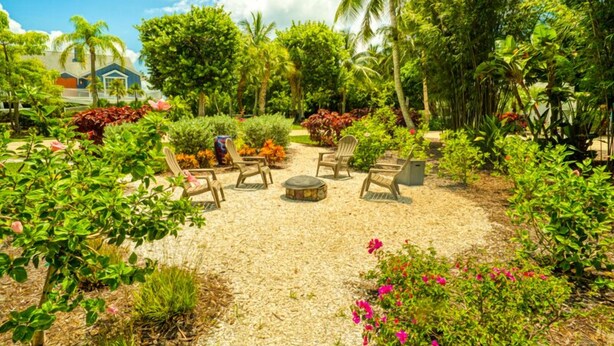 A garden with a seating area, palm trees, and a house in the background. - Baywatch Cabin- Boat Dock on the Channel (Captiva)