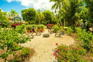 Ein Garten mit Sitzgelegenheit, Palmen und einem Haus im Hintergrund.