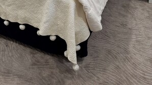 Een bed met een witte quilt, twee bruine kussens en een blauw gestreept hoofdeinde.