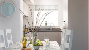 Une table à manger ornée d’un vase rempli de branches, d’un saladier de pommes et de verres à vin.