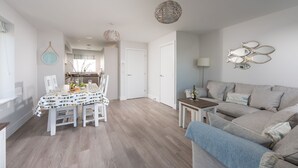 Un salon moderne avec un canapé gris, une table à manger avec des chaises, et une cuisine en arrière-plan.