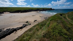 Une plage bordée d’une côte rocheuse, avec des zones herbeuses et un ciel bleu dégagé.