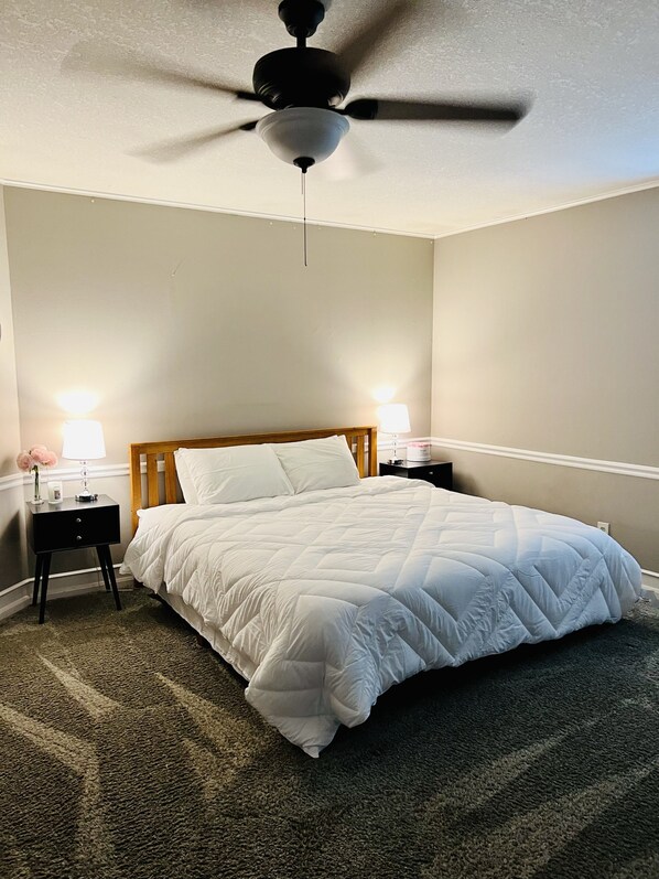 A bedroom with a bed, two bedside tables with lamps, a ceiling fan, and a carpeted floor.