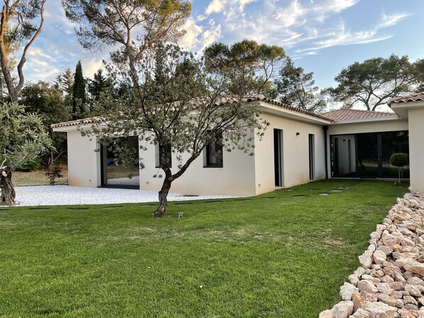Une maison moderne avec une pelouse bien entretenue, un arbre et un mur en pierre.