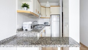 A modern kitchen with granite countertops, white cabinets, a built-in microwave, and a stainless steel refrigerator. - Home2Book Sea Side El Medano (El Medano)