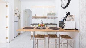 A kitchen with white cabinets, a wooden table, and a clock on the wall. - Home2Book Jable Beach Apartment (Morro Jable)