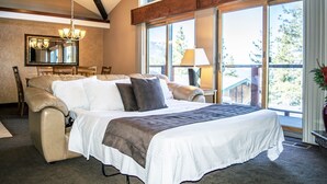 Ein geräumiges Schlafzimmer mit einem großen Bett, einer Sitzecke mit Sofa und Sesseln, einem Esstisch und einem Balkon mit Blick ins Freie.