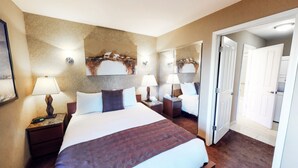 Ein Hotelzimmer mit einem großen Bett, zwei Nachttischen mit Lampen, einem Spiegel und einer Tür zu einem weiteren Raum.