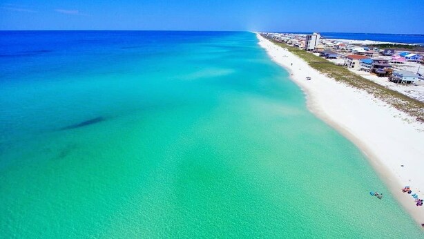 An aerial view of a beach with clear turquoise waters, a white sandy shore, and buildings along the coastline. - 🌟 New 🌟 Fun Mid-Century Modern Beachside Condo🏝🐠 (Pensacola Beach)
