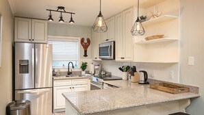A modern kitchen with stainless steel appliances, a granite countertop, and pendant lighting. - 🌟 New 🌟 Fun Mid-Century Modern Beachside Condo🏝🐠 (Pensacola Beach)