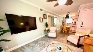 A modern living room with a flat-screen TV, a round coffee table, and a dining area with yellow chairs. - 🌟 New 🌟 Fun Mid-Century Modern Beachside Condo🏝🐠 (Pensacola Beach)