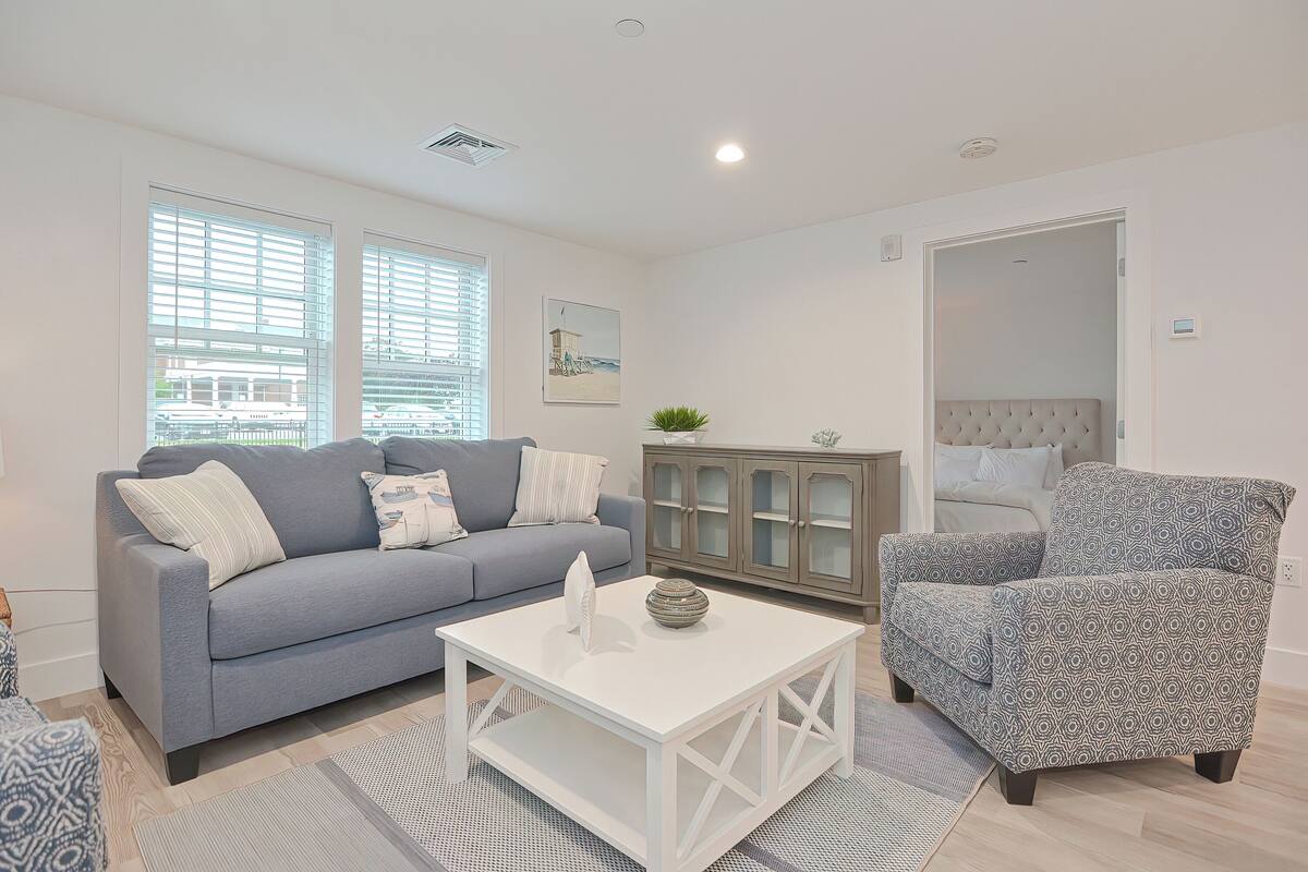 A living room with a grey sofa, a patterned armchair, a white coffee table, and a cabinet with glass doors.
