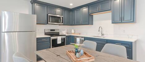 A modern kitchen with blue cabinets, stainless steel appliances, and a wooden dining table with a tray of decorative items.