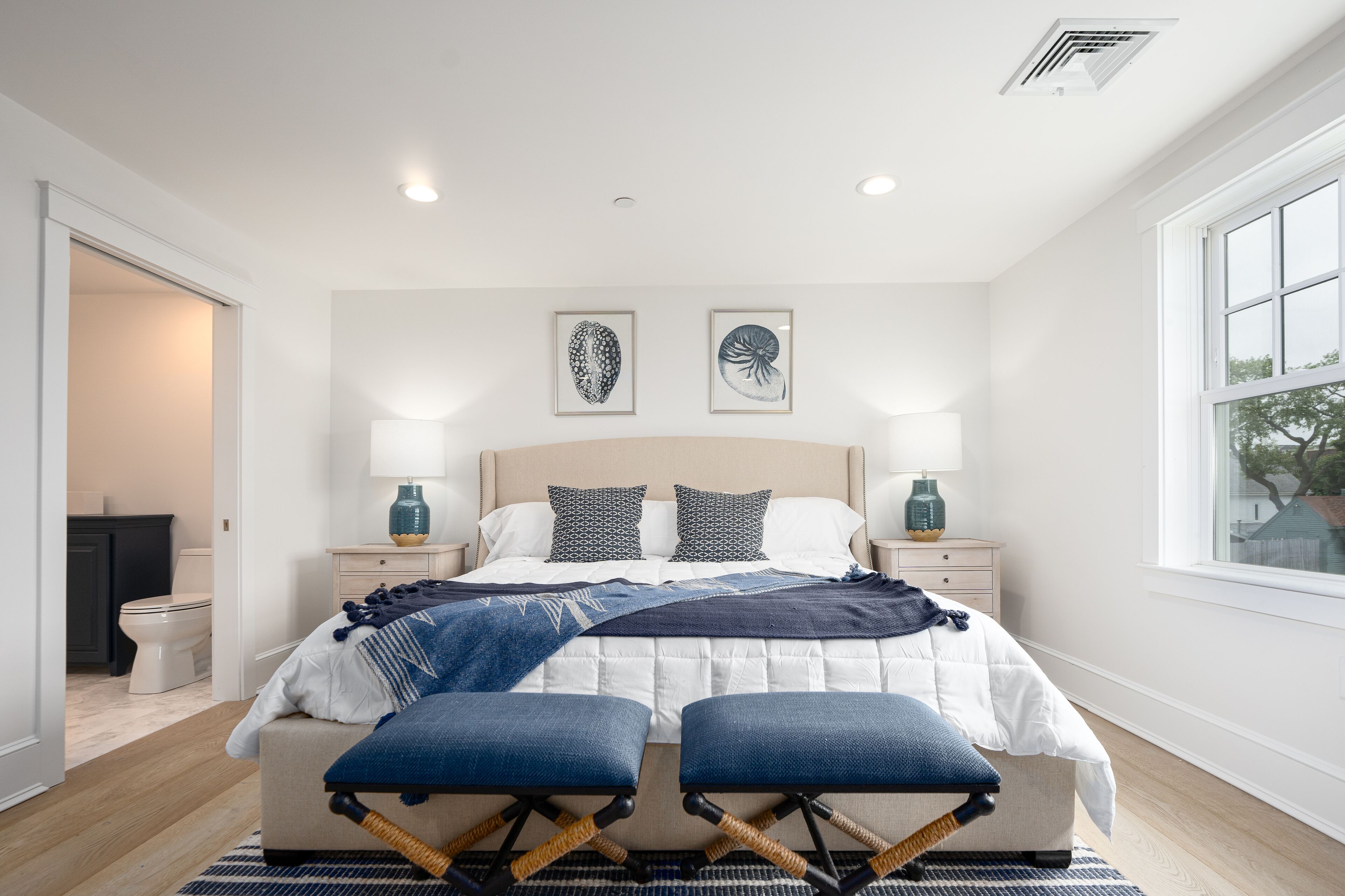 A bedroom with a bed, two bedside tables, a window, and a door leading to the bathroom.